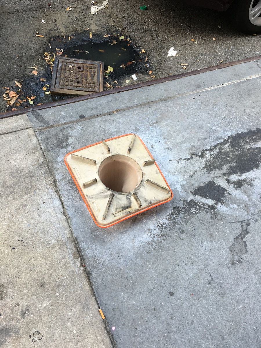 Cone fully inserted into a sidewalk hole, nearly flush with surface.