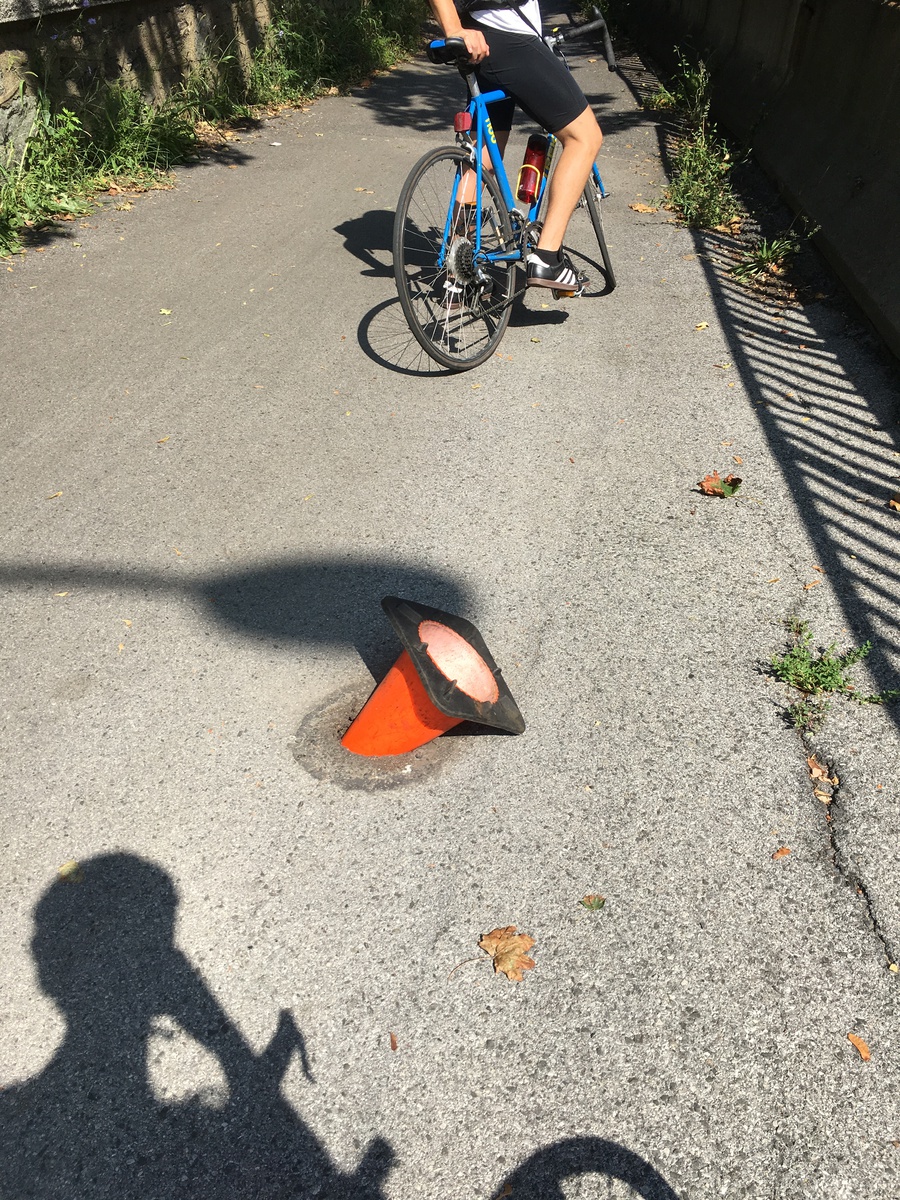 Cone partially inserted into hole in a bike path.