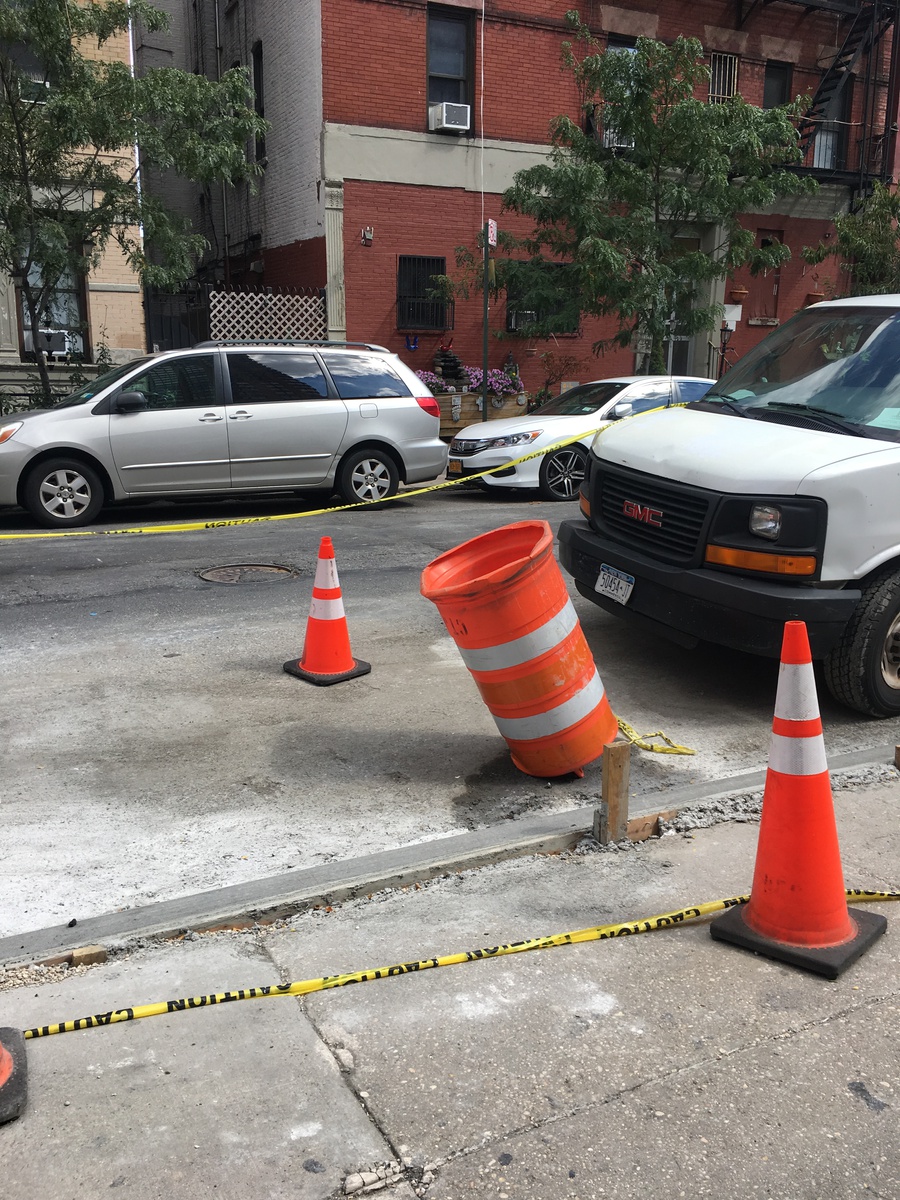 Inverted road work barrel on freshly-poured concrete, surrounded by two safety cones.
